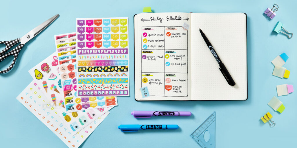 Bullet journal student planner on a blue background surrounded by school supplies. Featured planner supplies include Avery UltraTabs, Hi Liters, Marks A Lot ultrafine permanent markers and student planner stickers.