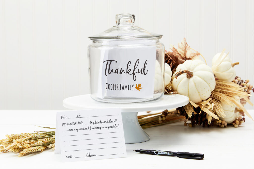 A beautiful white autumnal display on a white wooden table with white pumpkins and dried wheat featuring a gratitude jar made with clear Avery labels and Avery cards.