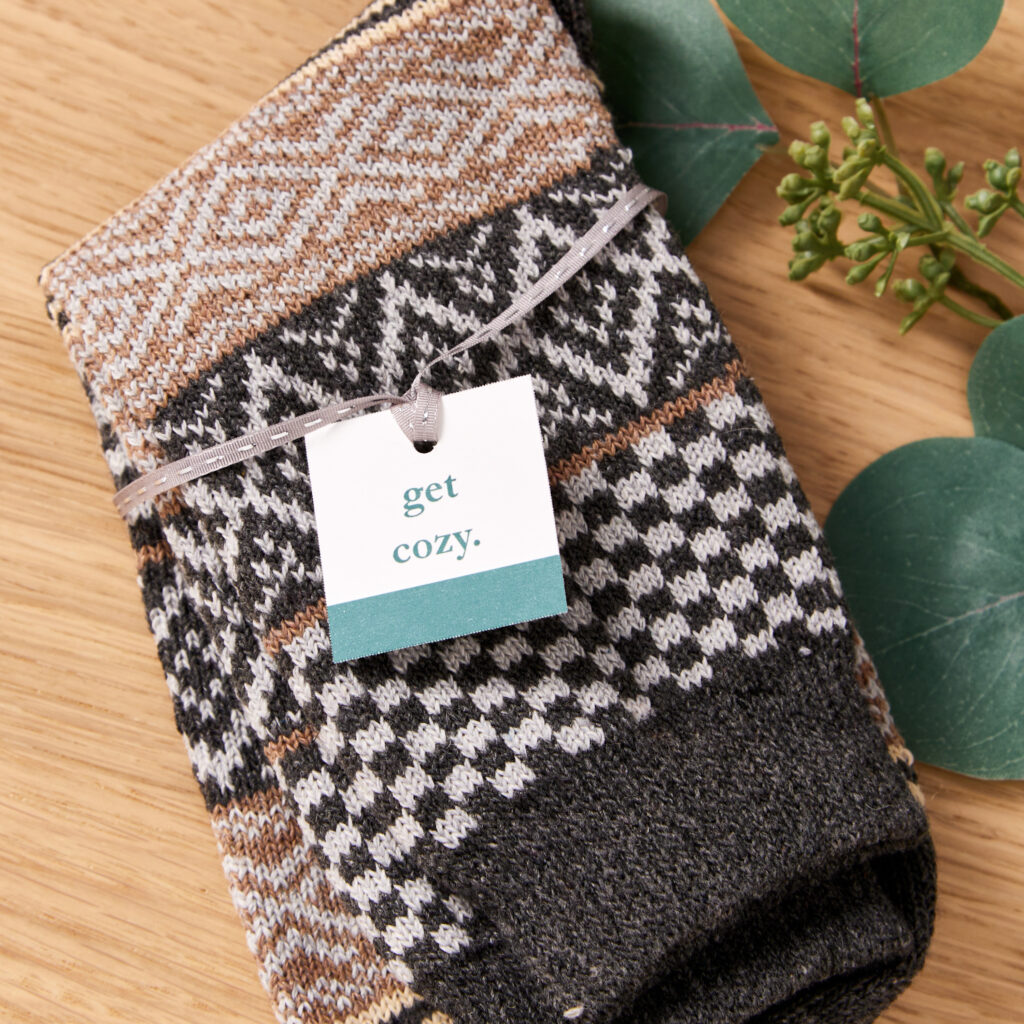 A pair of thick, cozy socks tied together with an elegant, thin ribbon with a custom-printed Avery square tag.