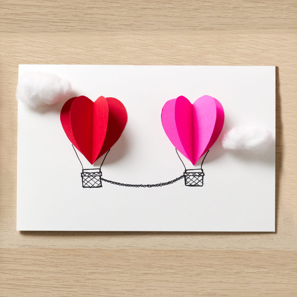 3D paper hearts and cotton ball "clouds" are glued on a blank Avery card to make Valentine's Day hot hair balloons.