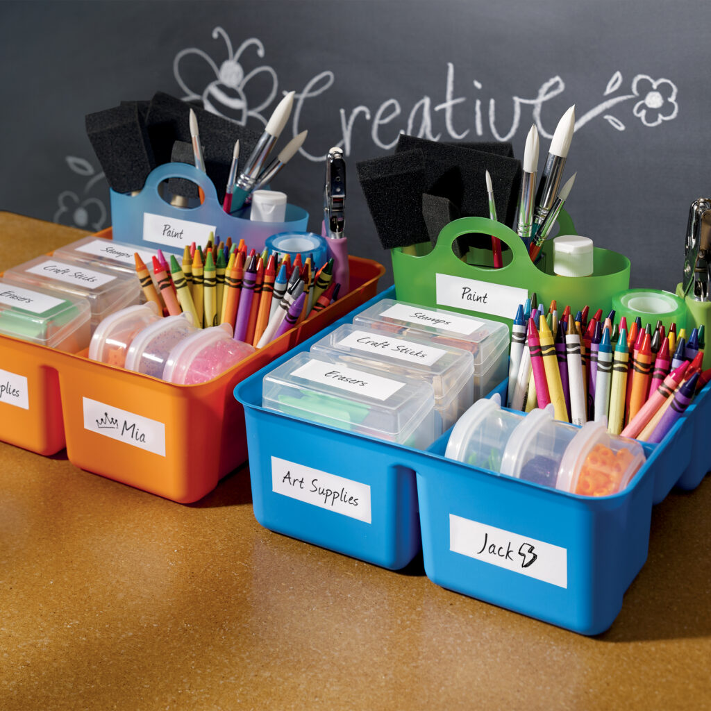 A picture of plastic caddies in front of a classroom chalkboard that says, "Creative" in white chalk. The bins are filled with various art supplies and labeled with Avery 5520 waterproof address labels.